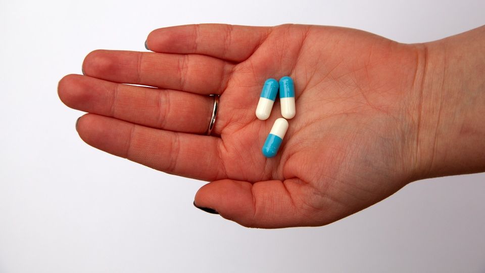 Blue and white capsules resting in an open hand against a plain background.