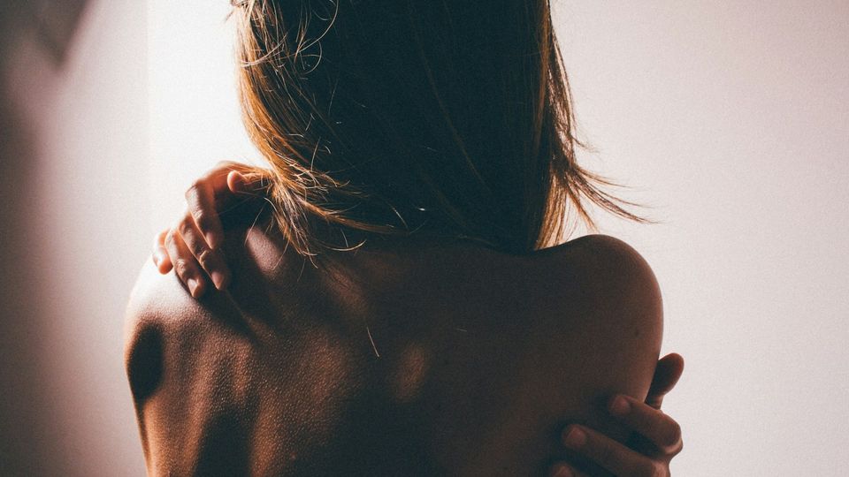 Woman holding her shoulder and upper back in soft natural light.