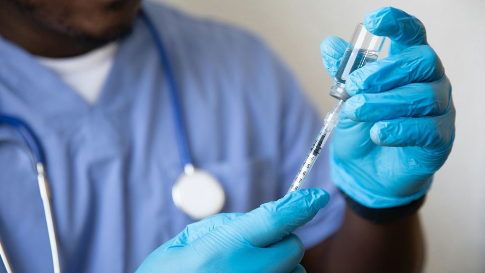 Healthcare worker preparing a vaccine injection with syringe and vial in gloved hands.