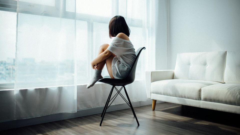 Woman sitting alone by a window in a quiet room.