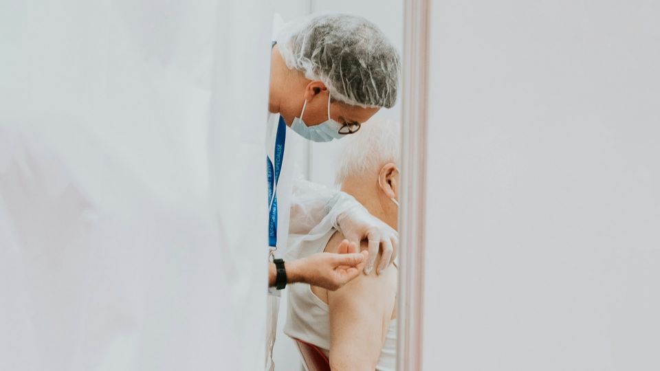 Side-view of a healthcare professional administering a vaccine injection into the arm of an elderly patient.
