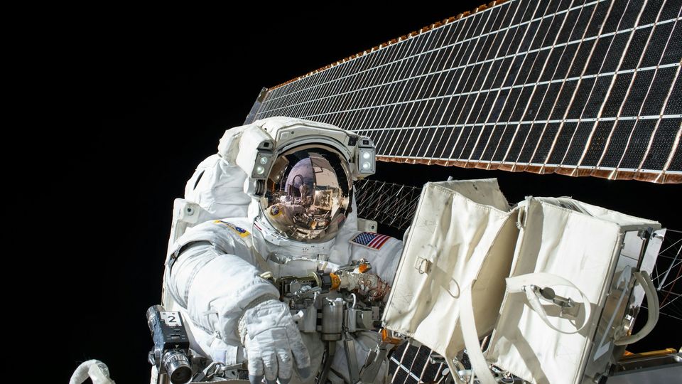 Astronaut conducting a spacewalk outside the International Space Station with solar panels.