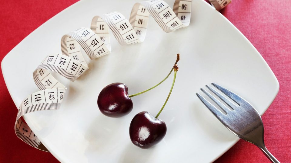 Birds-eye view of a measuring tape, cherries, and fork all placed on a plate.