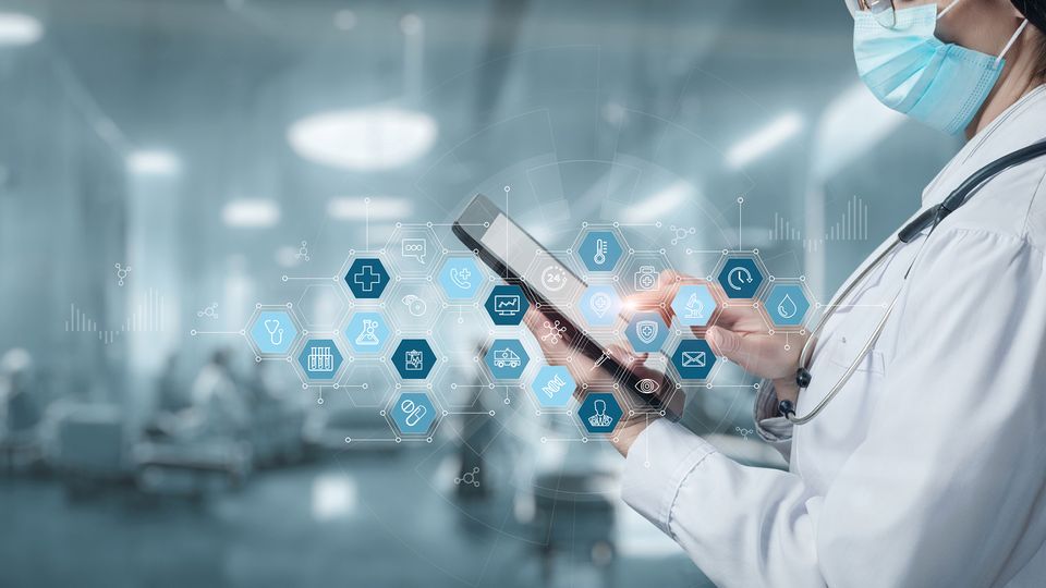 A clinician holds a tablet with icons relating to data in healthcare floating above it.