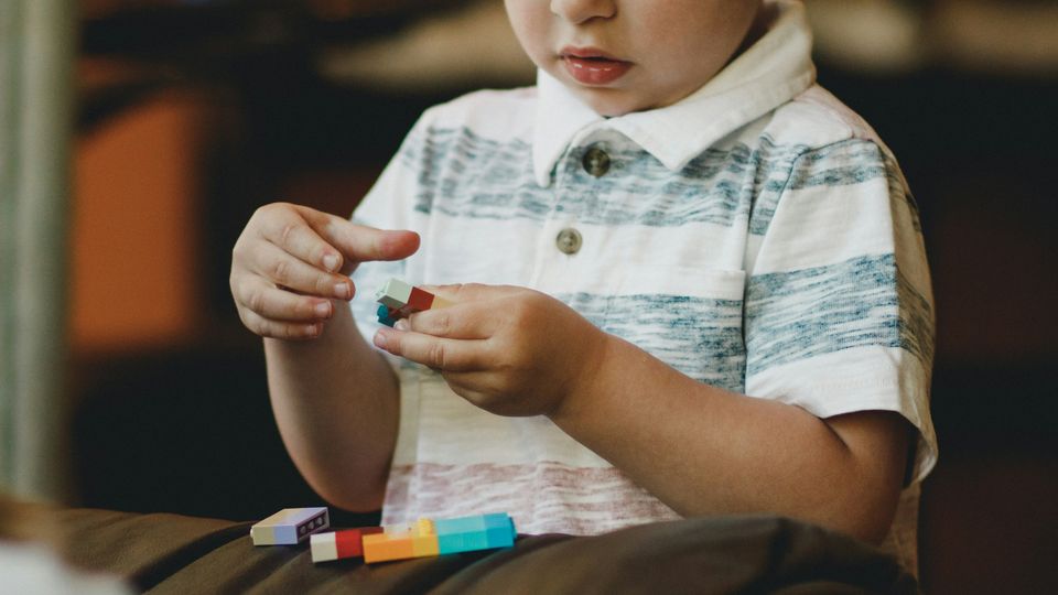 A young child holding toy bricks in his hands, with more bricks placed on a sofa beneath his hands.