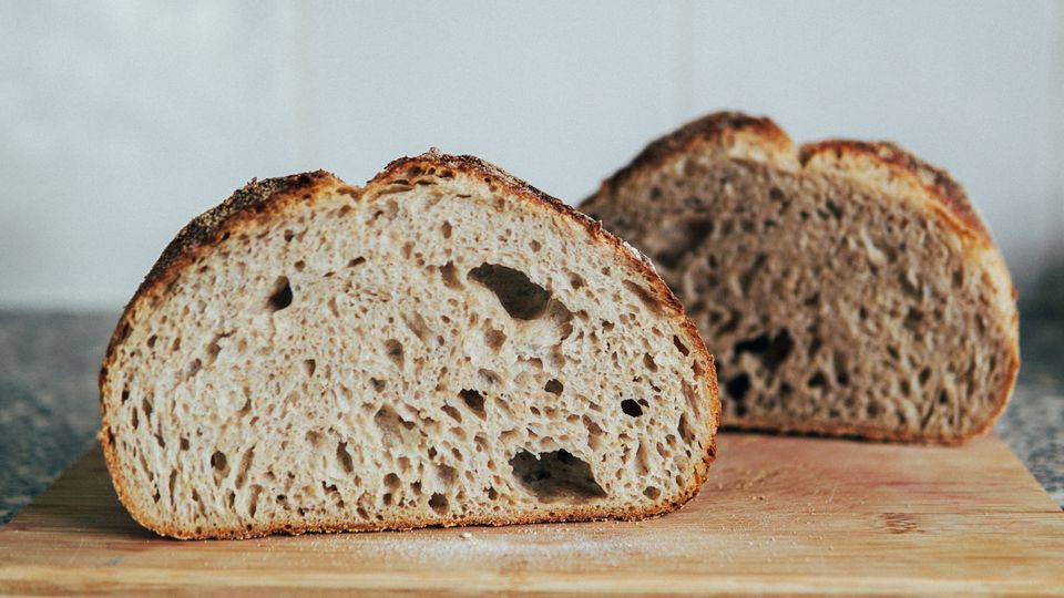 A loaf of sourdough bread, cut in half on a wooden chopping board.