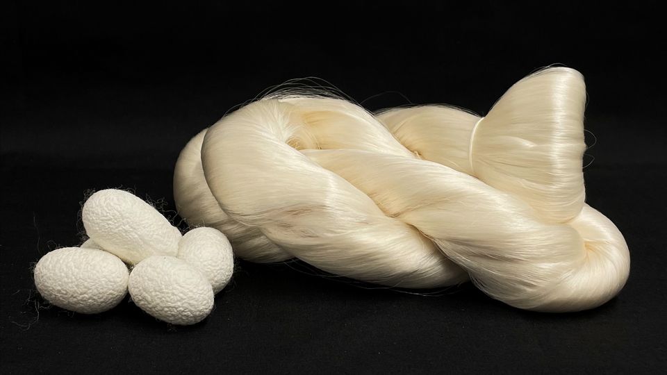 A pile of cocoons, next to a large reel of spun silk fibers.