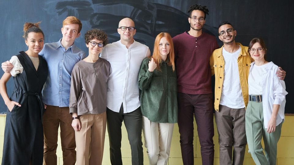 A diverse group of people, standing in front of a chalkboard.
