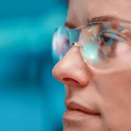 Close-up of scientist wearing safety glasses with digital data reflected, against blue background.