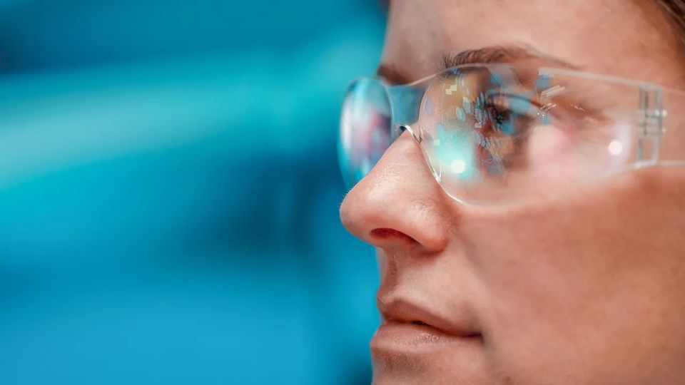 Close-up of scientist wearing safety glasses with digital data reflected, against blue background.