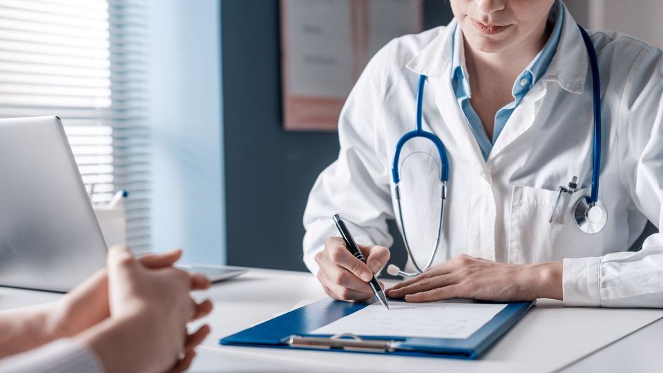 Healthcare professional with stethoscope writing on clipboard during a medical consultation.