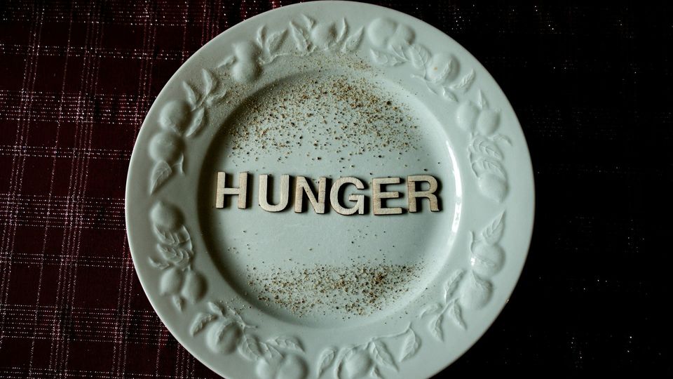 The word "HUNGER" spelled in wooden letters on an empty green dinner plate.