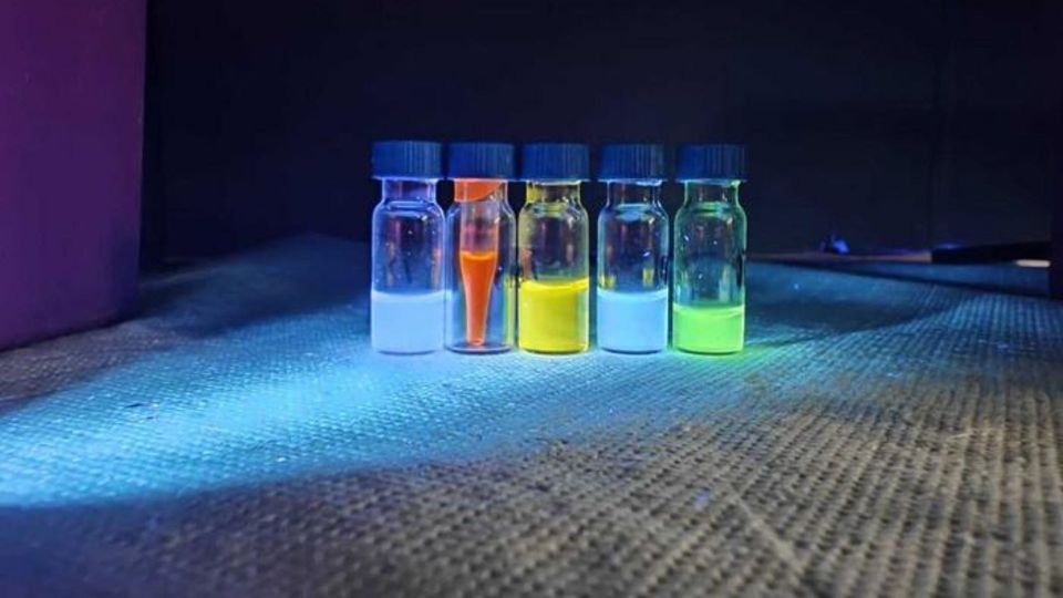 Glowing luminescent dye samples in laboratory vials under ultraviolet light.