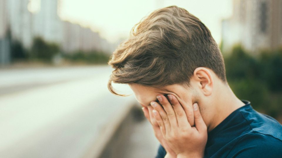 Teen boy covering his face with his hands outdoors, showing tiredness.