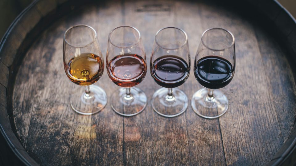 Four different wines of different colours, lined up on the top of a wooden barrel.