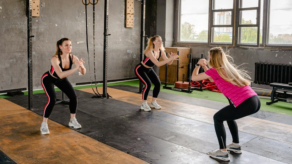 Three women performing squat exercises together in a gym.