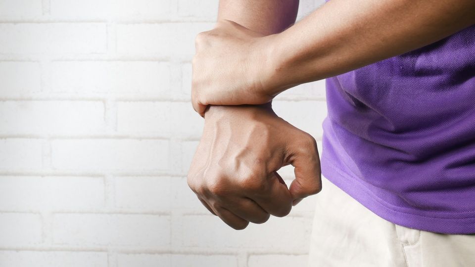 Person wearing a purple t-shirt gripping their wrist, with their fist clenched.