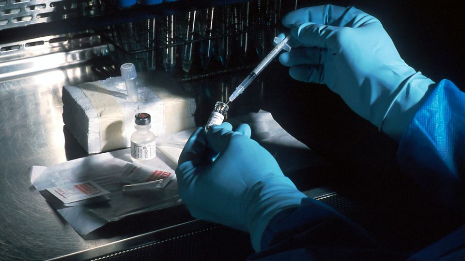 Vaccine vial being prepared with a syringe in a laboratory setting.