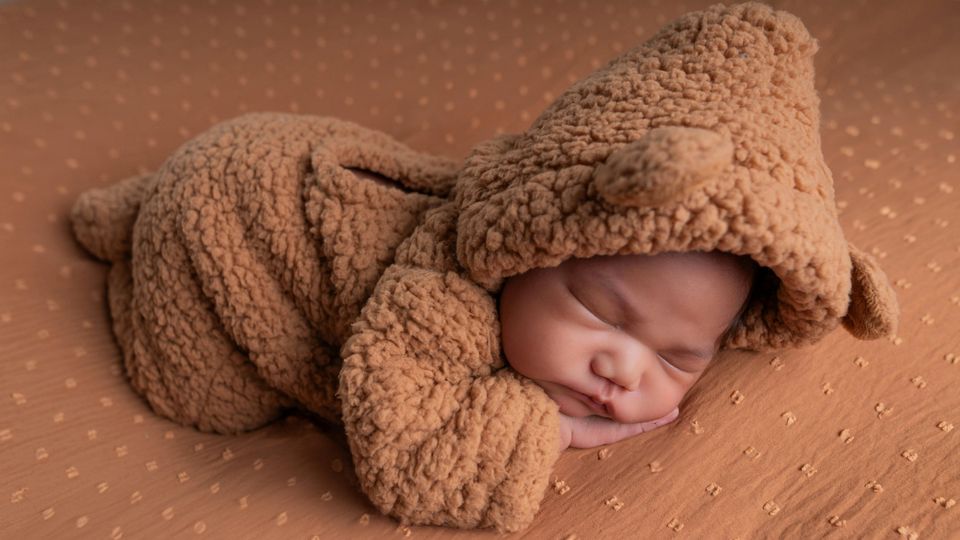 Sleeping newborn baby wrapped in a soft bear-themed outfit.