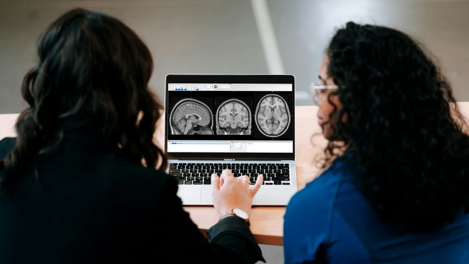 Two female researchers looking at a laptop, reviewing brain scans on the screen.