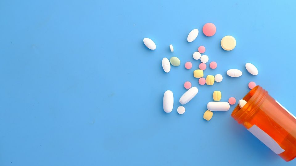 Assorted pills and tablets spilling from a prescription bottle on a blue background.