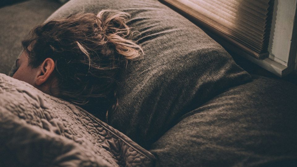 Girl sleeping under a blanket, with her head rested on a pillow beside a window.