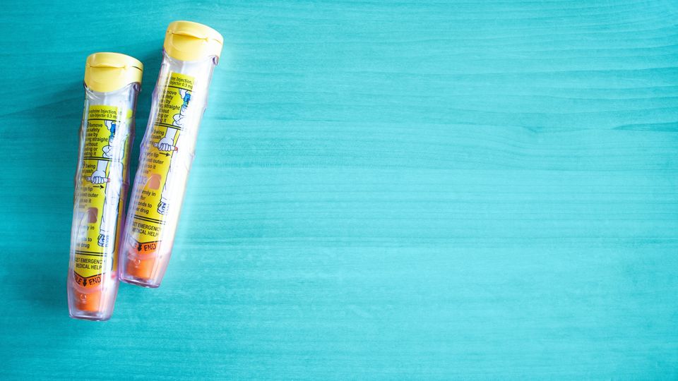 Two yellow adrenaline pens in clear cases on a teal background, with labels and orange safety tips visible.