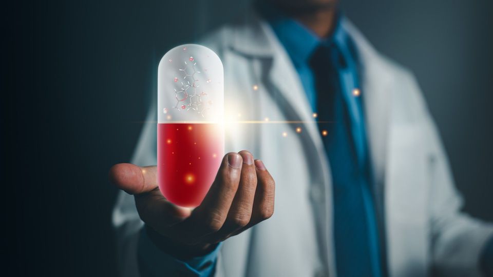 Scientist in a white coat holding an oversized glowing red and white medicinal capsule.