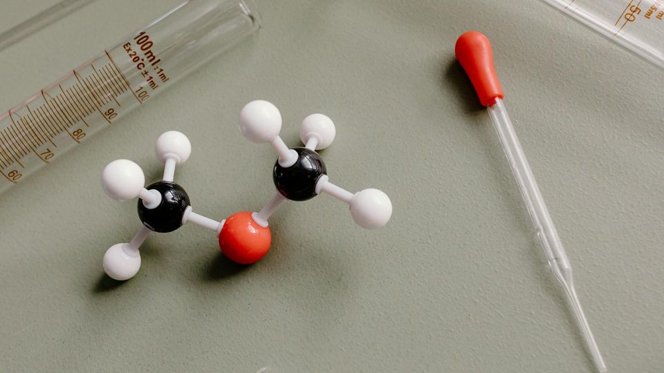Molecular model and laboratory dropper beside scientific glassware.