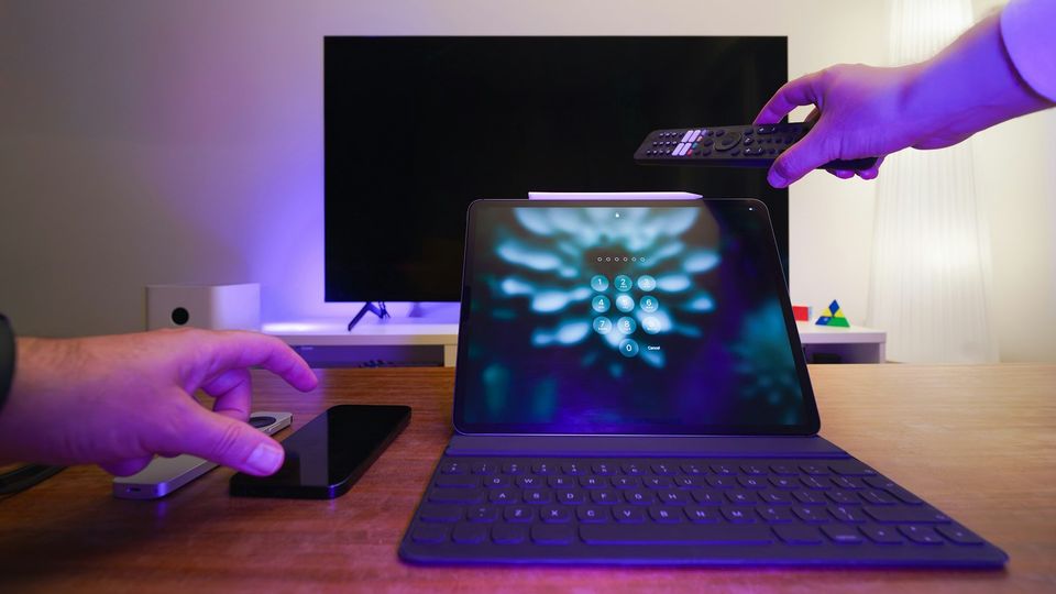 Tablet, smartphone, remote control, and television in a smart home entertainment setup.