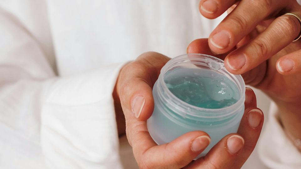 A person holding a cosmetic container with one hand, while reaching in for product with the other hand.