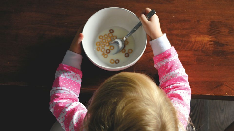 Child eating cereal with milk from a bowl at the breakfast table.