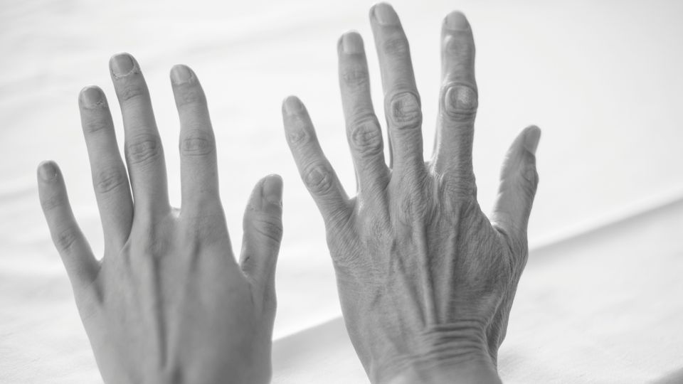 Black and white image of two hands held up next to each other, one is youthful and the other is aged.