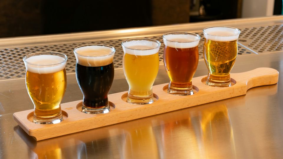 A flight of different beers in tasting glasses on a wooden plank.