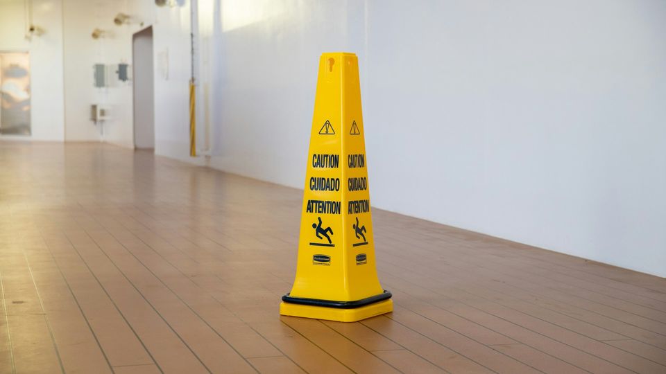 Yellow caution cone warning of a wet floor in an indoor hallway to prevent slip hazards.