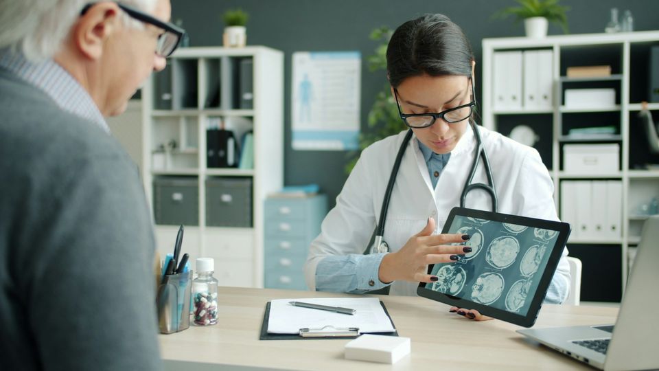Doctor reviewing brain scan images on a tablet while sat opposite a patient during a medical consultation.