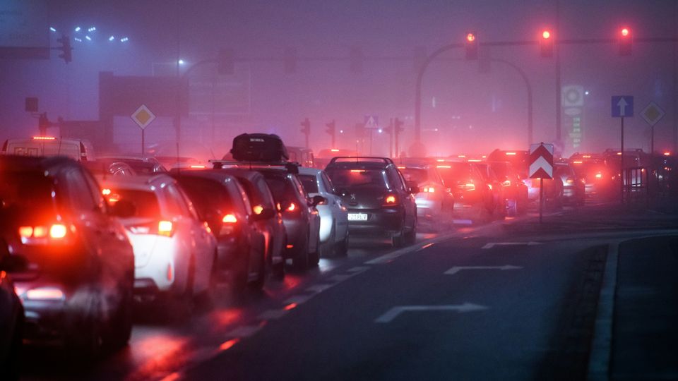 A queue of cars in standstill traffic, in a smog-filled city at night.