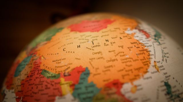 Close-up of a globe focusing on China which is pictured in a yellow and bordered by countries in various colors. 