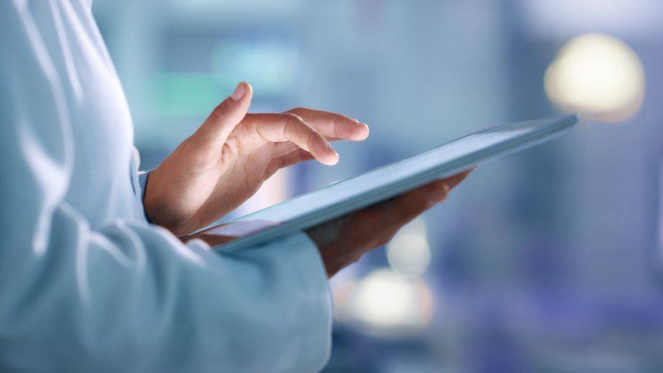 Close-up of a scientist's hands holding and using a tablet in a clinical setting.
