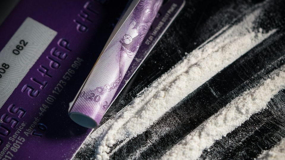 Close-up of credit card and rolled banknote beside lines of white powder.