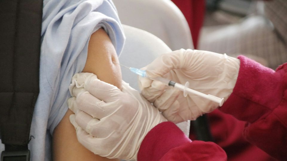 Healthcare worker wearing gloves administering a vaccine injection into the upper arm of a patient.