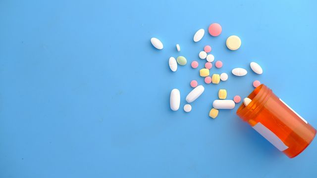 Assorted prescription pills and tablets spilled from an orange medication bottle on a blue background. 
