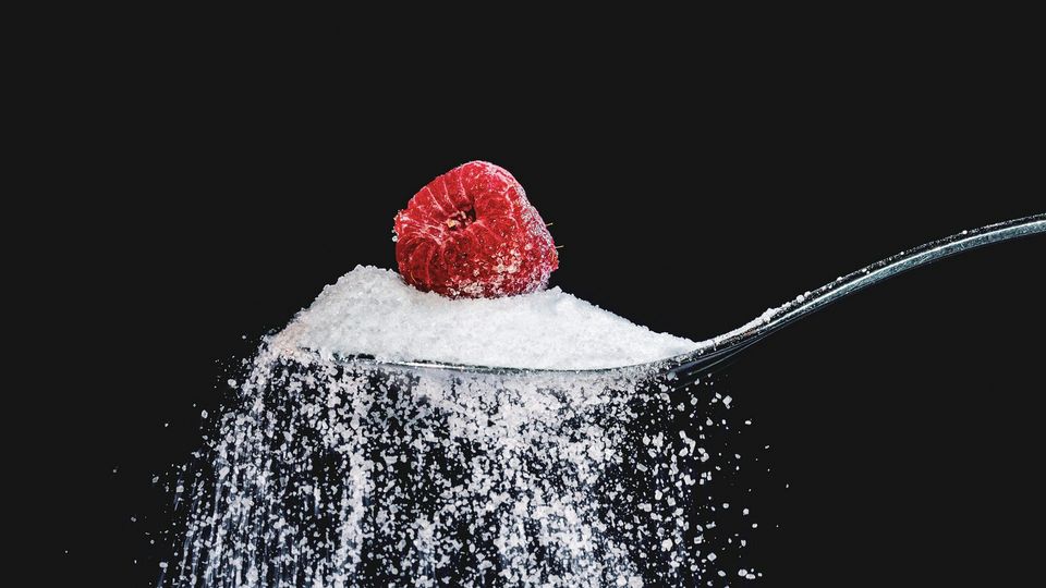A spoonful of sugar with a single raspberry balanced on top of it.
