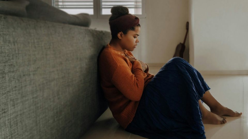 An anxious girl sits on the floor clutching her chest during an apparent panic attack.