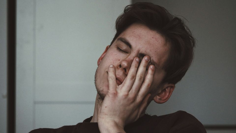 Close-up of a tired young man sleeping or resting with his hand covering his face and eyes.