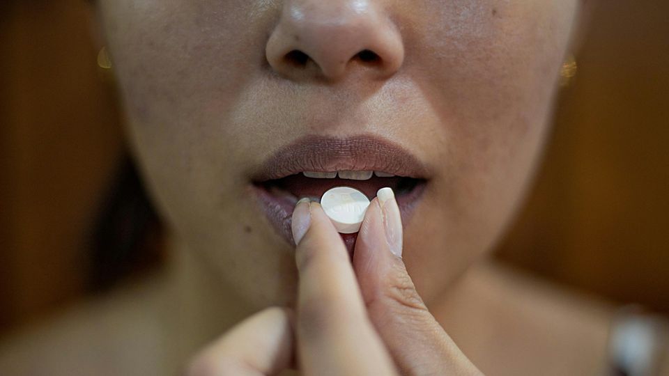 A close-up view of a women placing a white, round pill into her mouth.