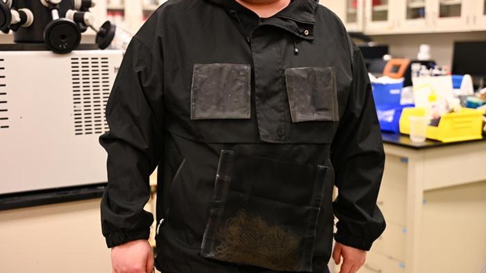 A man wearing a black jacket. The jacket has a number of dark gray detachable panels on the chest and stomach.