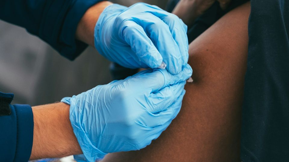 Healthcare worker wearing blue gloves administering a vaccine injection in a patient's upper arm.