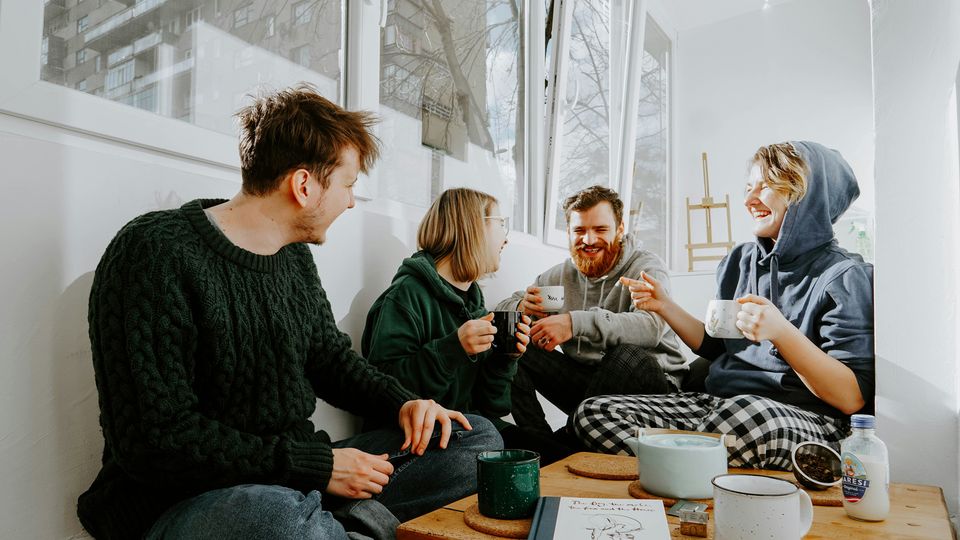 A group of cohabiting friends sat around a table laughing and drinking.