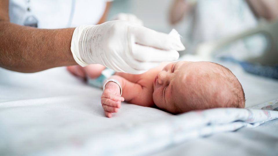 Newborn baby lying on a sheet being cared for by a healthcare professional.
